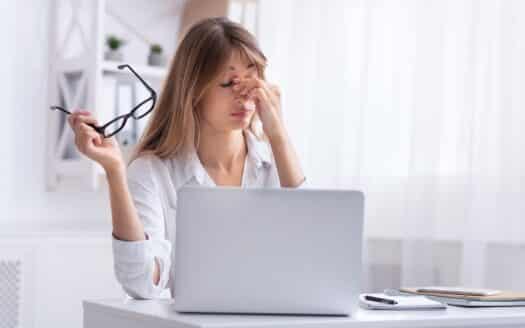 femme retirant ses lunettes devant un ordinateur pour illustrer la formation continue opticien ICO CMO sur la fatigue visuelle au travail : le rôle de l'opticien
