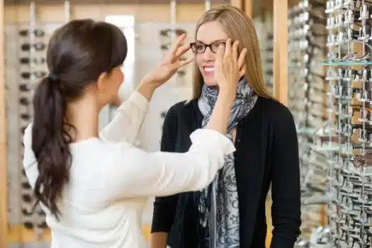 une femme essaie des lunettes dans un magasin l'optique pour illustrer la FAQ sur la reconversion pour devenir opticien conseils ICO ecole optique Paris Sud